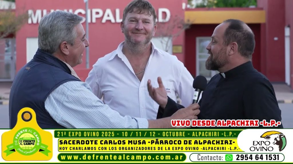 Tres hombres conversando frente al edificio municipal; un sacerdote y dos entrevistadores en la previa de la Expo Ovino.
